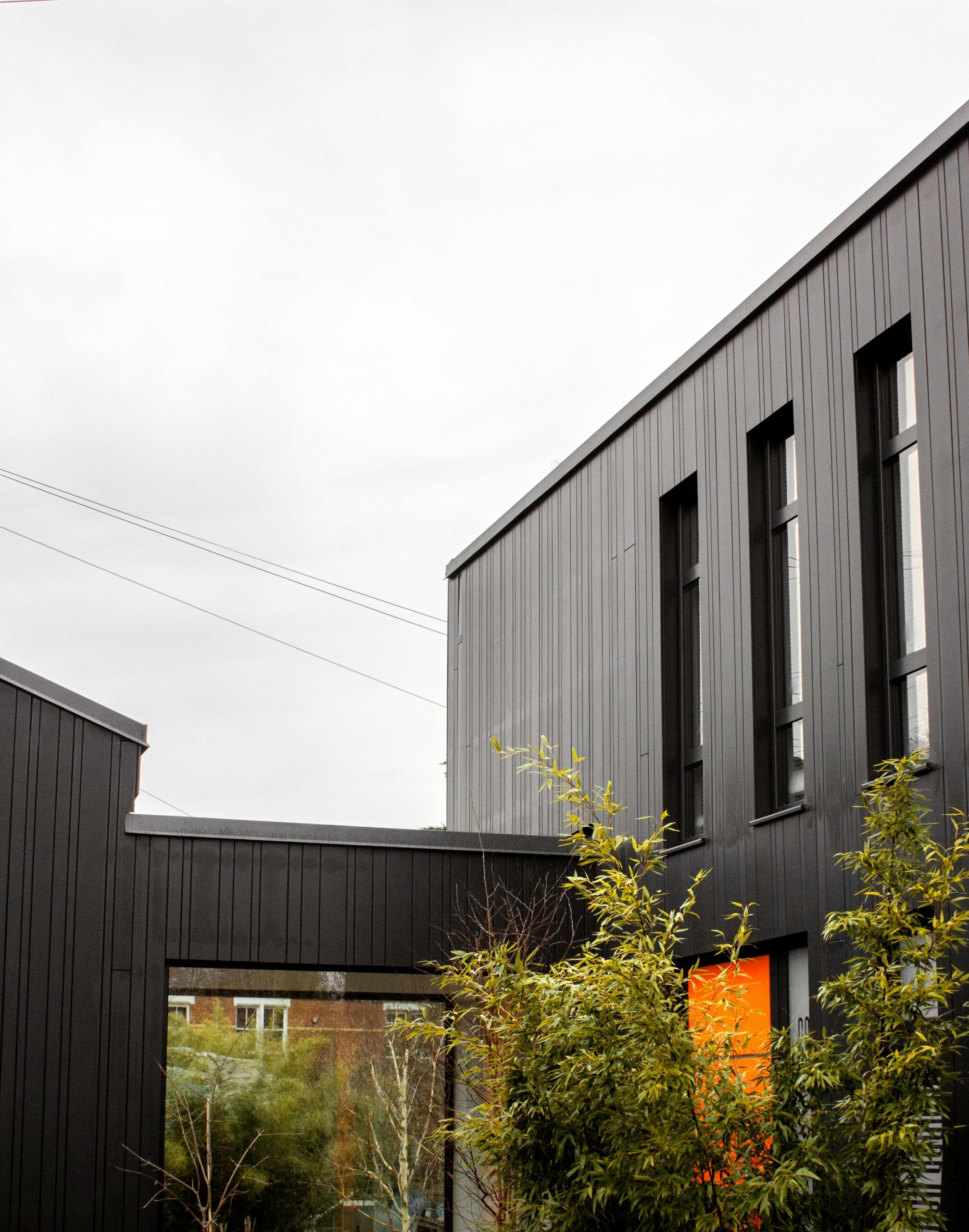 A contemporary black house with bold architecture and a striking orange door on an overcast day.